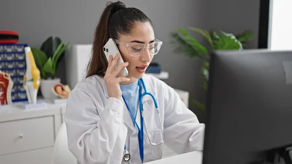 年轻美丽的惊慌失措的女医生在诊所用电脑用智能手机交谈 — 图库照片