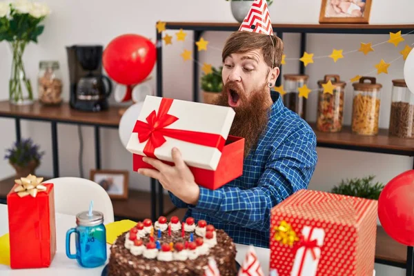 Young redhead man celebrating birthday unpacking gift at home