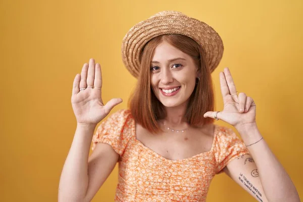 年轻的红头发女人站在黄色的背景上 头戴夏帽 手指指尖八号 面带微笑 自信而快乐 — 图库照片