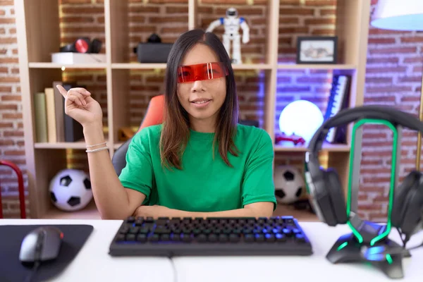 stock image Middle age chinese woman wearing virtual reality glasses with a big smile on face, pointing with hand and finger to the side looking at the camera. 