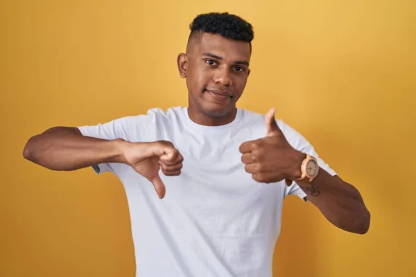 Молодой Латиноамериканец Стоящий Жёлтом Фоне Делающий Большие Пальцы Вверх Вниз — стоковое фото