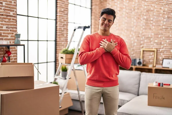 Hispanic man moving to a new home smiling with hands on chest, eyes closed with grateful gesture on face. health concept.