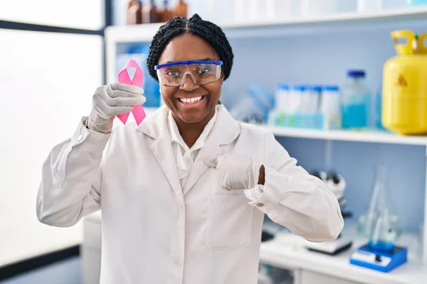 アフリカ系アメリカ人女性研究室で働くピンクリボンを手に指を指差して笑顔で誇りに思う — ストック写真