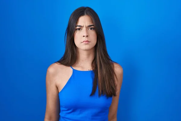 西班牙裔女人站在蓝色背景的旁边 怀疑和紧张 因为问题皱着眉头 消极的人 — 图库照片