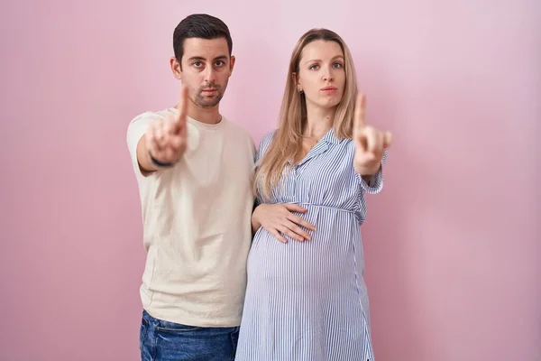 Casal Jovem Esperando Bebê Sobre Fundo Rosa Apontando Com Dedo — Fotografia de Stock