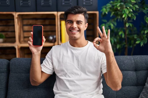 拿着智能手机的拉美裔男子 手握手机 显示空白屏幕 手拿着手签 微笑着表示友善的手势 展示着极好的象征 — 图库照片