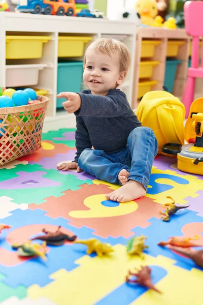 Sevimli Sarışın Çocuk Yerde Oturmuş Parmağını Anaokulunu Işaret Ediyor — Stok fotoğraf