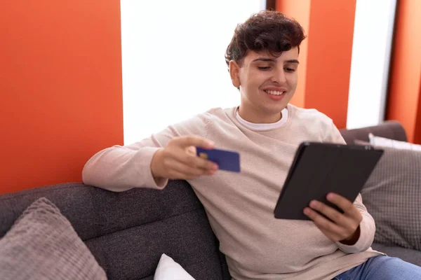 Non binary man using touchpad and credit card sitting on sofa at home