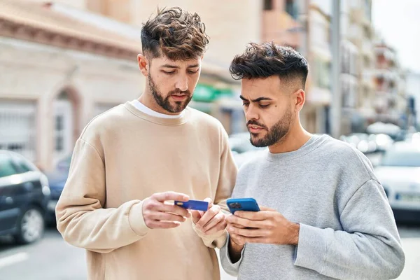 年轻夫妇一起站在街上用智能手机和信用卡 — 图库照片