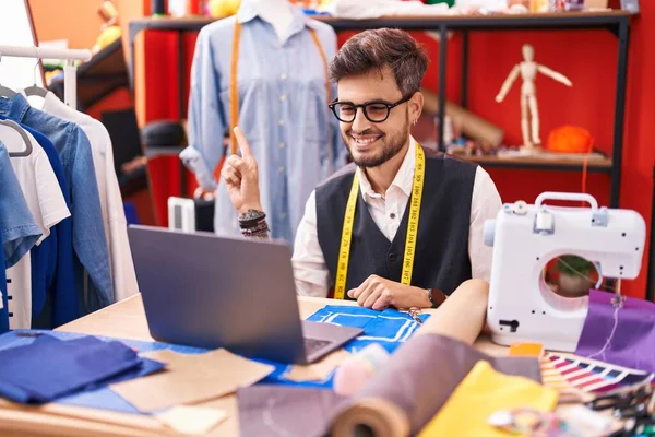 身穿纹身服装的年轻人在裁缝店用笔记本电脑设计服装 一边微笑着一边手指手画脚 — 图库照片