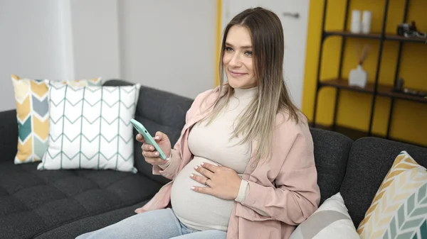 Jonge Zwangere Vrouw Met Smartphone Aanraken Buik Thuis — Stockfoto