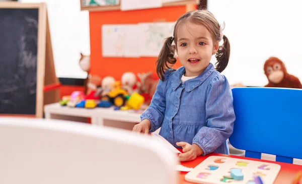 Entzückendes Hispanisches Mädchen Lächelt Selbstbewusst Kindergarten Auf Dem Boden Sitzend Stockbild