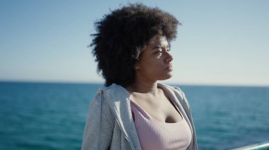 Afrika kökenli Amerikalı kadın deniz kenarında ciddi bir ifadeyle duruyor.