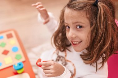 Adorable hispanic girl playing with maths puzzle game sitting on table at kindergarten