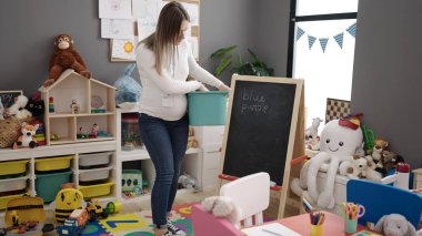 Anaokulunda sırtı ağrıyan genç hamile kadın anaokulu öğretmeni oyuncak topluyor.