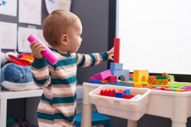 Sevimli beyaz bebek anaokulunda duran inşaat bloklarıyla oynuyor.