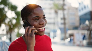 Afro-Amerikalı kadın akıllı telefondan konuşuyor. Sokakta gülümsüyor.