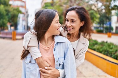 Woman and girl mother and daughter hugging each other at park