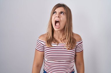 Young hispanic woman standing over isolated background angry and mad screaming frustrated and furious, shouting with anger. rage and aggressive concept. 