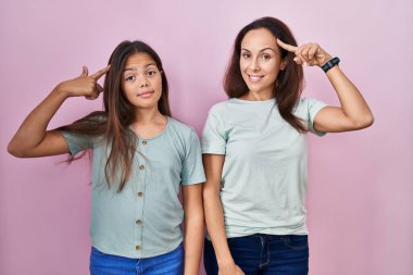 Pembe arka planda duran genç anne ve kız gülümseyerek tek parmağıyla kafasını işaret ediyor, harika bir fikir ya da düşünce, iyi bir hafıza. 