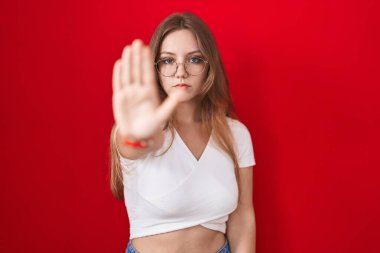 Kırmızı arka planda duran genç beyaz kadın avucunun içi gibi şarkı söylemeyi kesiyor. Yüzünde olumsuz ve ciddi bir jest olan uyarı ifadesi. 