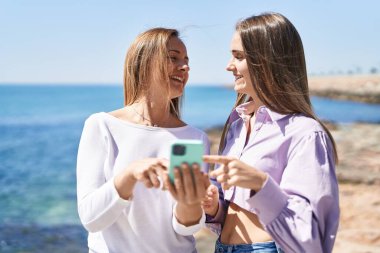 Two women mother and daughter using smartphone at seaside