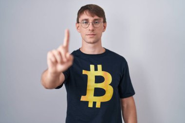 Bitcoin tişörtlü, beyaz, sarışın bir adam parmağını kaldırmış ve kızgın bir ifade takınıyor. 