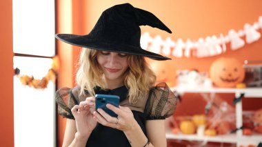 Young blonde woman wearing halloween costume using smartphone at home