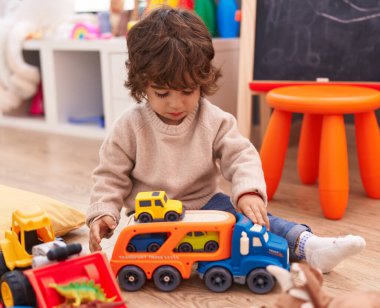 Anaokulunda yerde oturan sevimli İspanyol çocuk araba oyuncağıyla oynuyor.