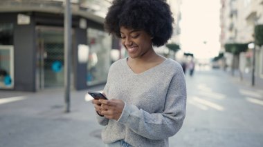 Afro-Amerikalı kadın sokakta akıllı telefon kullanarak kendine güveniyor.