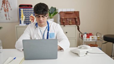 Genç İspanyol doktor klinikte dizüstü bilgisayar kullanıyor.