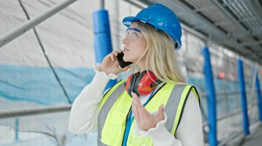 Sarışın genç bir mimar sokakta akıllı telefondan konuşuyor.