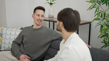 İki erkek kanepede oturup konuşuyor.