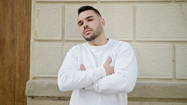 Ciddi bir ifadeyle ve kollarını kavuşturarak sokakta dikilen İspanyol genç bir adam.