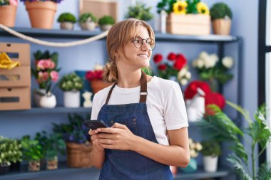 Young blonde girl florist smiling confident using smartphone at florist