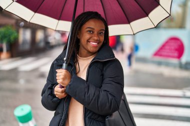 African american woman smiling confident using umbrella at street