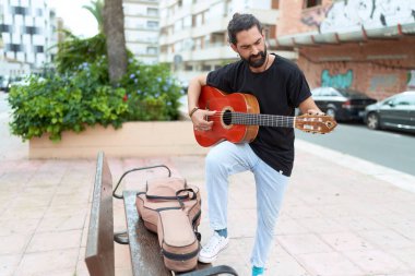 Young hispanic man musician playing classical guitar at park