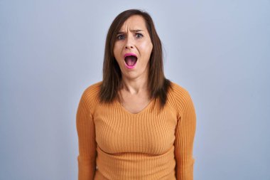 Orta yaşlı esmer kadın turuncu kazak giymiş kızgın ve kızgın bağırıyor sinirli ve öfkeli, öfkeyle bağırıyor. öfke ve agresif konsept. 