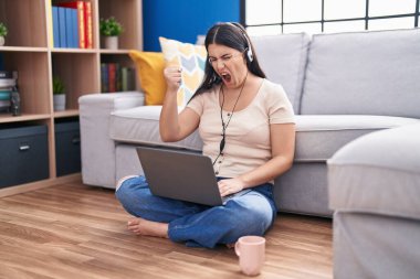 Evde dizüstü bilgisayar kullanan genç İspanyol kadın öfkeyle bağırıyor, öfkeyle bağırıyor ve el kaldırıyor. 