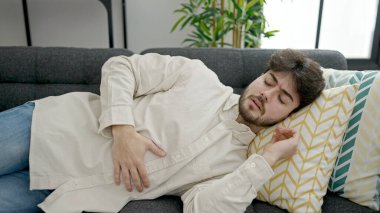 Genç İspanyol adam mide ağrısı çekiyor. Evdeki kanepede yatıyor.
