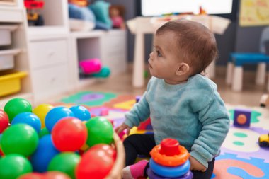 Anaokulunda yerde oturmuş taşaklarıyla oynayan sevimli İspanyol bebek.