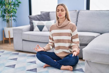 Yoga yapan genç bir kadın evde yerde oturuyor.