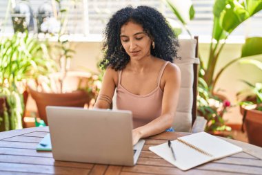 Young hispanic woman using laptop sitting on table at home terrace