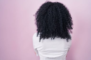 Pembe arka planda duran kıvırcık saçlı İspanyol kadın kollarını kavuşturup arkaya bakıyor. 