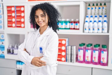 Young hispanic woman pharmacist smiling confident standing with arms crossed gesture at pharmacy