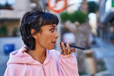 Gülümseyen genç bir kadın caddedeki akıllı telefondan konuşuyor.