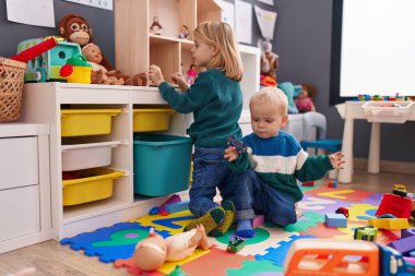 Sevimli bir çocuk ve kız yerde oturup anaokulunda oynuyorlar.