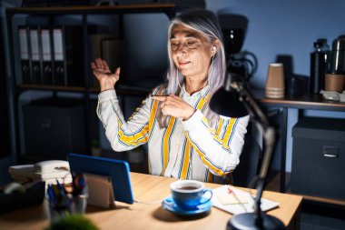 Gri saçlı orta yaşlı bir kadın gece ofiste çalışırken kameraya hayret ediyor ve gülümsüyordu. Elleri ve parmaklarıyla gösteriyordu.. 