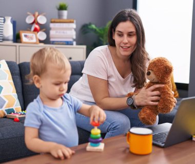 Anne ve oğlu evde oyuncak ayı tutuyor.