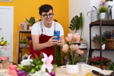 Non binary man florist make photo to flowers by smartphone at flower shop